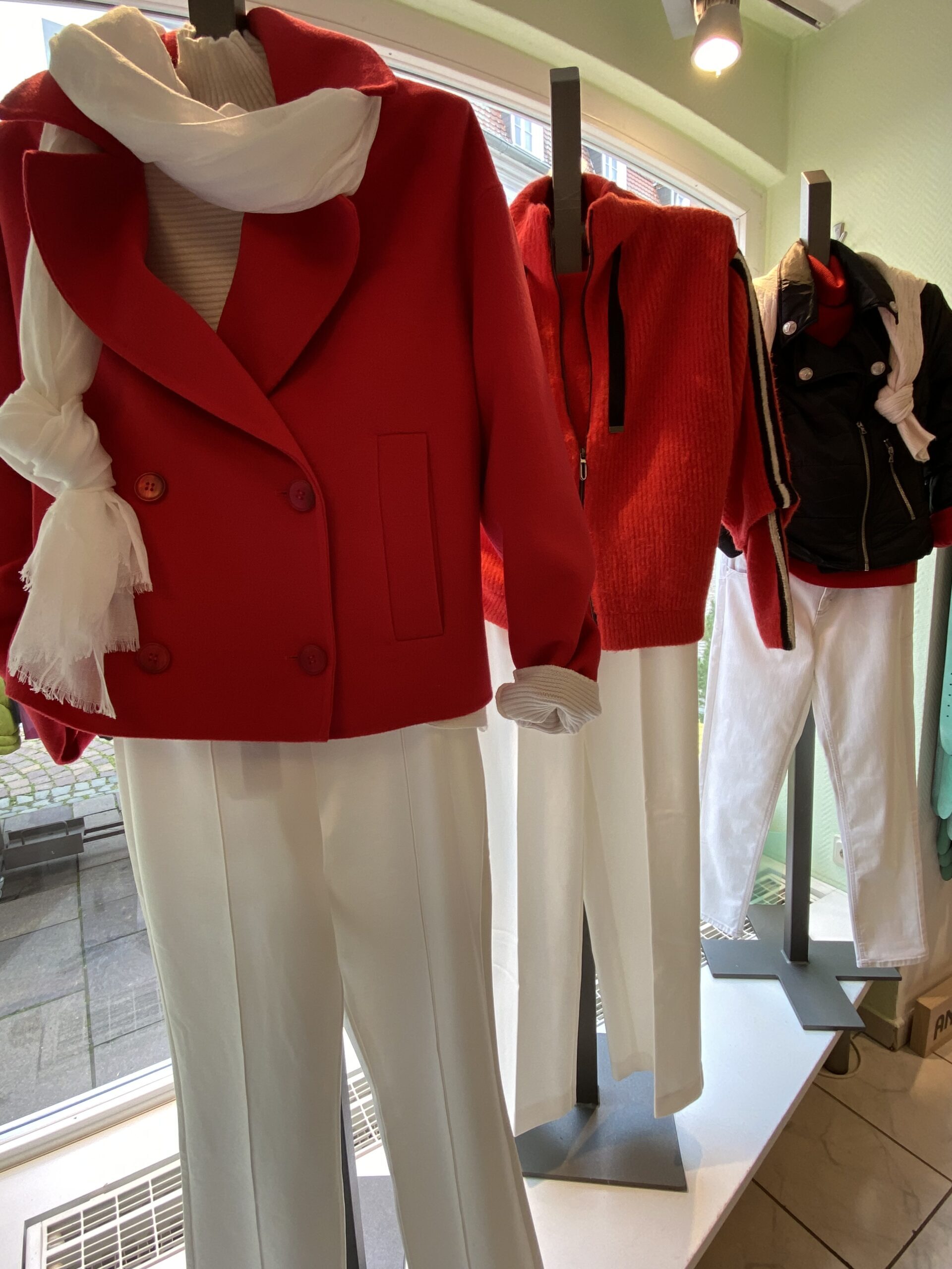 Schaufenster mit roten Jacken, weißen Schals und Hosen. Elegante Mode in lebendigen Farben.